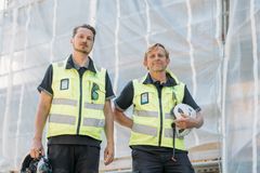 Mikko Heikkilä ja Marko Kahilainen julkisivuremontissa olevan rakennuksen edustalla, rakennustelineiden edessä. Heillä on turvaliivit yllä ja kypärät kädessä.