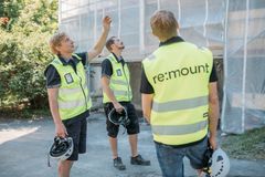 Kolme henkilöä julkisivuremontissa olevan rakennuksen edustalla, rakennustelineiden edessä. Heillä on turvalliivit yllään ja he katsovat ylöspäin, kun yksi henkilö osoittaa jotakin korkealla olevaa.