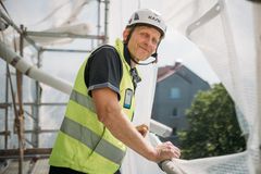 Marko Kahilainen seisoo julkisivuremontin työmaan rakennustelineillä. Korkeutta on muutama kerros. Kuva on otettu sivulta, ja Kahilainen on kääntänyt katseensa kohti kameraa. Taustalla näkyy asuinkerrostalo.