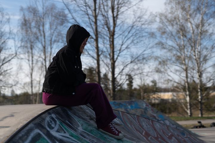 Tyttö istuu huppu päässä skeittiparkissa rampin reunuksella ja katsoo eteenpäin.