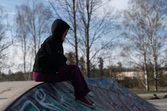 En flicka sitter i en skatepark med huvan uppdragen och tittar rakt fram.