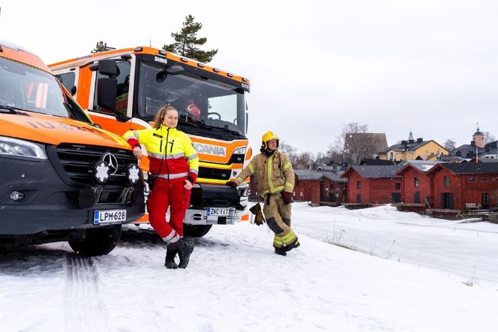 Ensihoitaja ja palomies seisovat ambulanssin ja paloauton edessä Porvoonjoen rannalla.