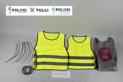 Kuvassa nippusiteitä, teippiä, huomioliivejä, muovipussi.