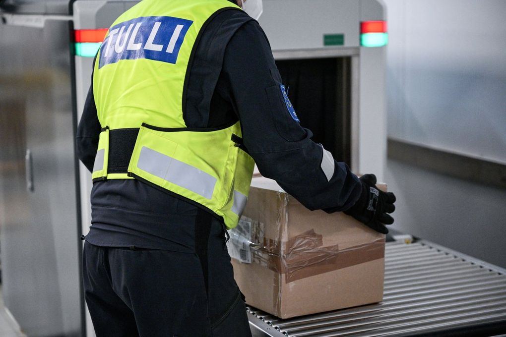 Tullin työntekijä laittaa paketin läpivalaisulaitteeseen.