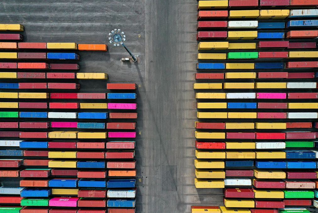 Flygbild av staplade containrar i olika färger på en containerterminal.