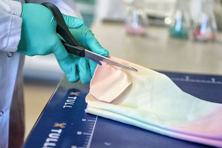 Laboratoriotyöntekijä leikkaa saksilla palasta lasten ulkohaalarista laboratoriossa.