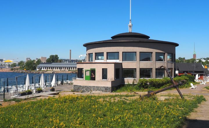 Valokuva HSS Paviljongista Helsingin Liuskasaaressa kauniina kesäpäivänä. Etualalla vihreää nurmikkoa ja taustalla merimaisema.