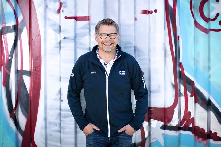 Toimitusjohtaja Juho Sihvonen värikkään seinän edessä hymyilemässä.