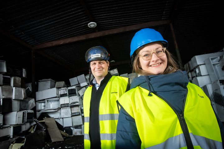 Olli Alanen ja Maija Hirsmäki keltaisissa huomioliiveissä ja suojakypärissä kierrätyslaitoksella