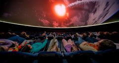Ihmiset istuvat tuoleilla planetaarion projisointikuvun alla katsellen simuloitua avaruusnäkymää, jossa meteori matkaa kohti maata.