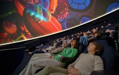 Ihmiset katsovat planetaariossa projisointukuvulla näkyvää animaatioelokuvaa.