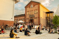 Maitokahvin värinen Tavara-aseman rakennus kuvattuna kesäillassa Uusi Tampereen aikaan. Pihalla istuskelee ihmisiä.