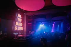 Valokuva Klubilta, jossa vietetään yökerhoiltaa. DJ:t soittavat musiikkia, ja ihmiset tanssivat sinertävässä valaistuksessa. Salin seinällä on punainen valokyltti, jossa lukee All you bleed is love.