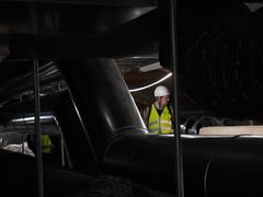 Valokuvassa näkyy isoja putkia ja valokaapeleita. Valaistus on tumma. Taustalla seisoo Tampereen Kulttuurikamarin ohjelmapäällikkö Janne Laurila pukeutuneena keltaiseen huomioliiviin ja työmaakypärään.