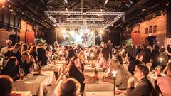 Valokuva Tullikamarin 30-vuotissyntymäpäiviltä. Pakkahuoneen saliin on katettu valkoisilla pöytäliinoilla koristeltuja illallispöytiä, joiden ääressä istuu juhlavieraita.