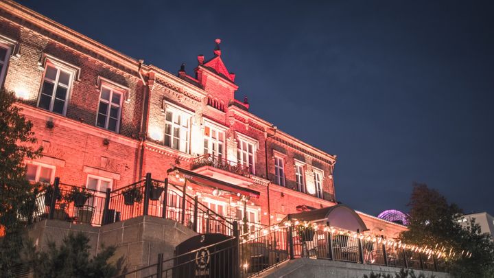 Tullikamari kuvattuna alaviistosta tummaa iltataivasta vasten. Rakennus hohtaa punertavan sävyisessä juhlavalaistuksessa.