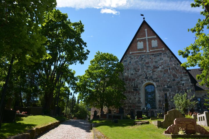 Esbo domkyrka med lummiga träd i solsken.