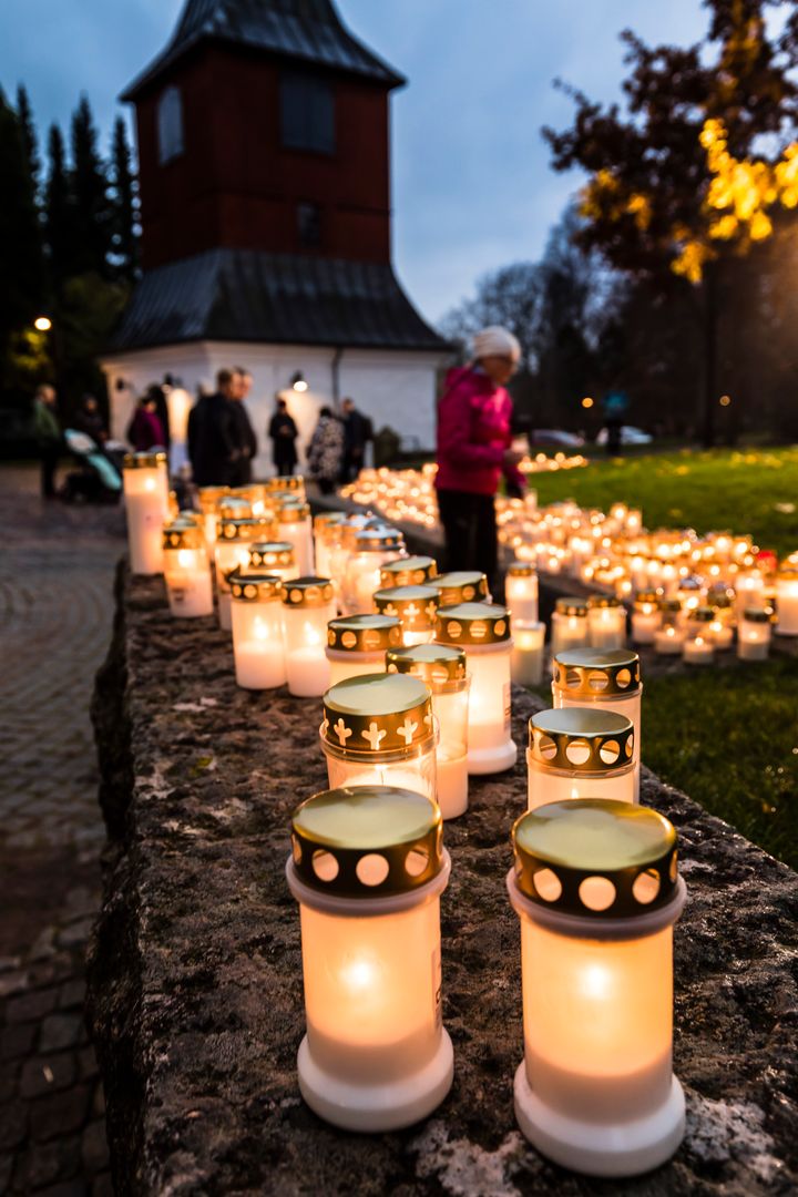 Klockstapeln vid Esbo domkyrka och tända ljus på murkrönet, i bakgrunden människor som tänder fler gravljus.