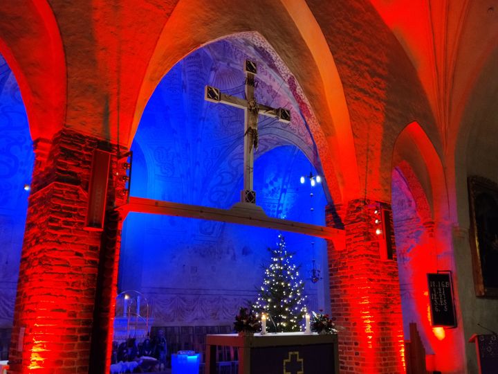 Röd belysning över valvbågen vid koret i Esbo domkyrka och blå belysning över altaret och en julgran som glimmar.