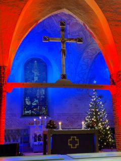 Röd beslysning över valvbågen i Esbo domkyrkas kor och blå belysninginnanför altarrundeln och en glimmande julgran.