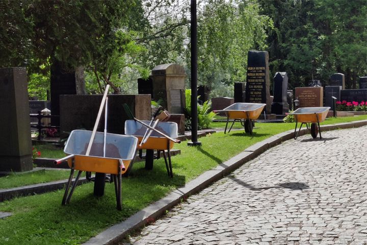 Fyra gula skottkärror står med redskap i på gravgårdens gräsmatta intill Esbo domkyrka.