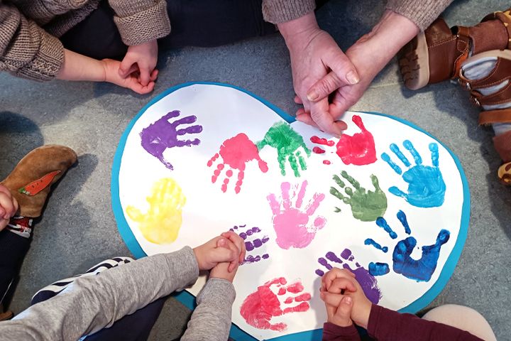 En vuxen persons och flera barns händer som trycker avtryck i färg med sina handflator på ett pappershjärta.