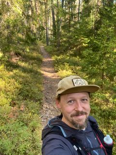 Heikki Lehti hymyilee metsäpolulla lippis päässä.