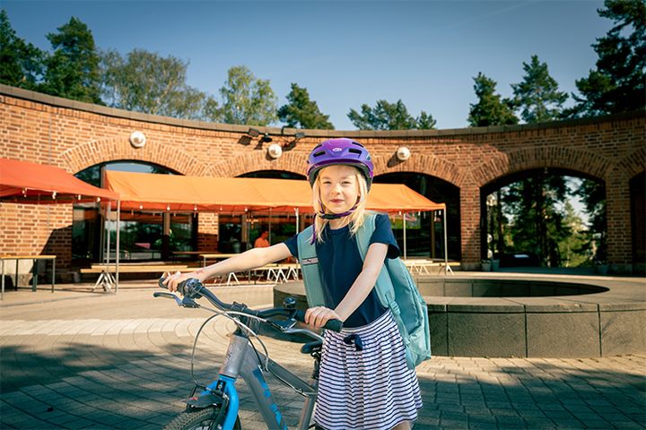 En förstaklassare med sin cykel och ryggsäck på gårdsplanen till Alberga kyrka.