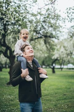 tyttö aikuisen harteilla kesäisessä puistossa