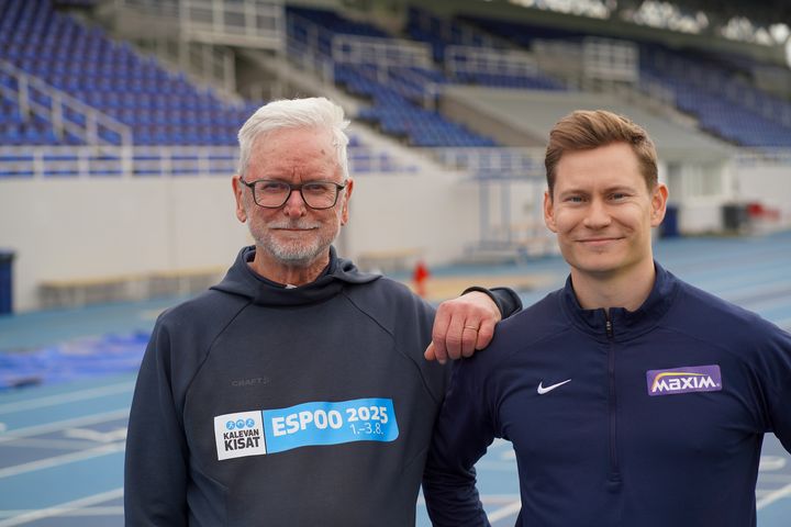 Två män står på en arena med läktare i bakgrunden.