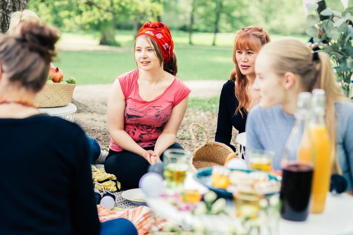 Joukko nuoria aikuisia istuu viltin päällä puistossa piknik-eväät edessään.