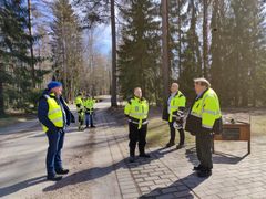 Flera män i gula arbetsrockar står i en klunga utomhus och diskuterar.