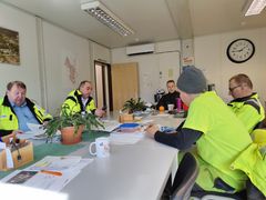 Flera personer sitter i gula arbetskläder runt ett mötesbord.