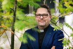 En man i prsätkrage står i grönskande omgivning.