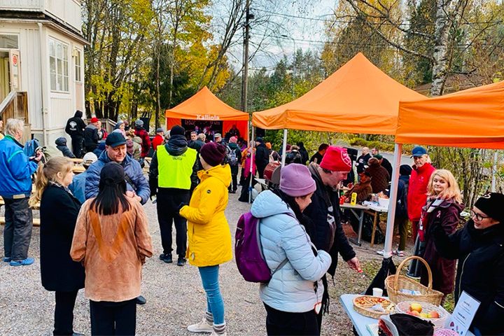 Tiotals personer står utomhus på gården intill en trävilla och tält med orangea tak är uppställda.