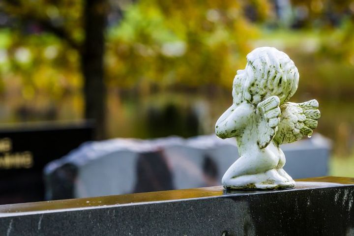 Närbild av änglastaty som sitter ovanpå en gravvård och i bakgrunden höstliga färger.