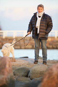 En kvinna i ytterkläder ute med sin hund vid en strand.