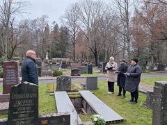 Flera personer i mörka kläder står på en begravningsplats vid en öppen grav.