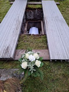 En vitdraperad kista i en öppen grav och en blombukett med vita blommor.