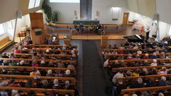 Kirkkosali ylhäältä päin kuvattuna, penkit täynnä ihmisiä, edessä meneillään paneelikeskustelu.