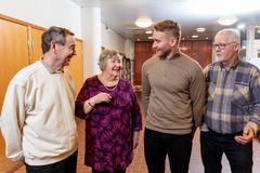 Neljä ihmistä seisoo rivissä, katsoo toisiaan ja hymyilee.