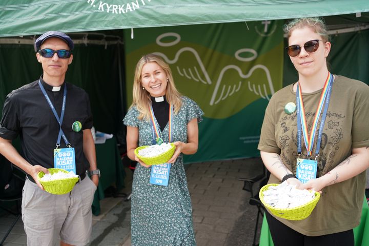 Kuvassa on kolme henkilöä ulkona teltan edessä käsissään korit.