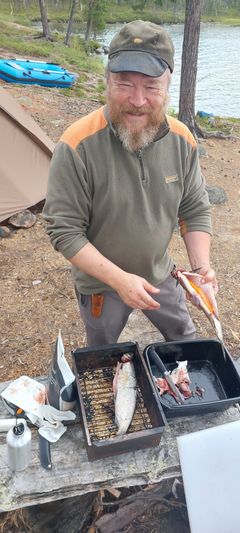Kuvassa on henkilö luonnossa veden äärellä kalansavustuslaatikko edessään.