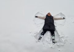 En mörkklädd kvinna ligger i snön och gör en snöängel med sin kropp och sina armar.