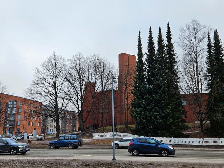 En röd stor tegelbyggnad som är en kyrka med biltrafik framför.