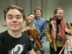 Kuvassa on neljä iloista muusikkoa harjoitustauolla.