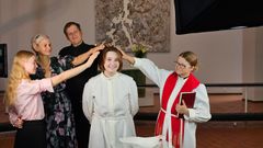 läheiset, kummit ja pappi siunaavat nuorta kastettavaa pitämällä käsiä hänen päänsä yllä