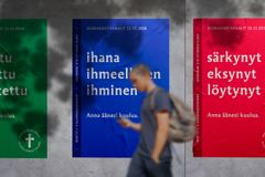 Tre affischer i olika färger med text. I bakgrunden går en person som är suddig.