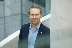 Mies hymyilee pukeutuneena pukuun ja seisoo sisätiloissa.