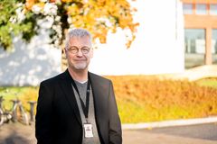 Kuvassa Olli-Pekka Ruuskanen seisoo ulkona syksyisessä maisemassa, taustalla puu ja rakennus.